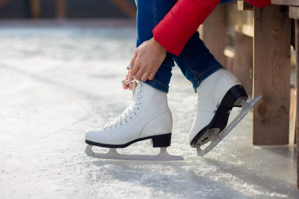 A girl is tying shoelaces on figured white skates on an ice rink